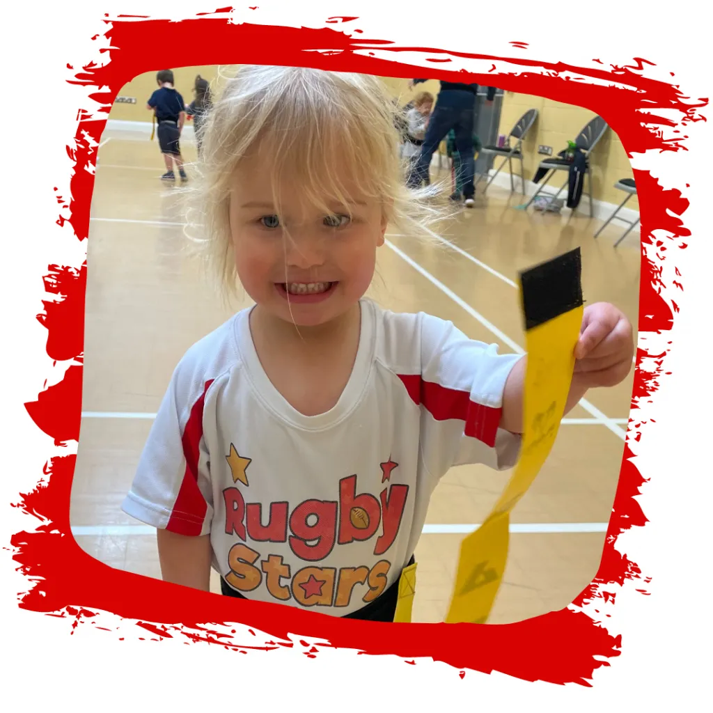 A smiling toddler in a Rugby Stars T-shirt playing in a Micros session in Kibworth and Market Harborough