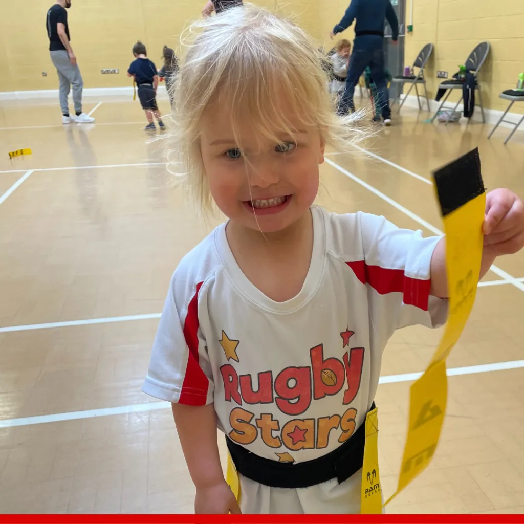 A smiling toddler playing Rugby Stars games in a sports hall